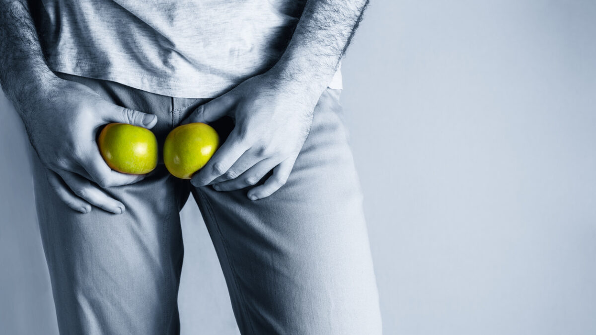 A man in beige jeans at the level of the genitals , holding a ripe and rotten apple. Disease for men. The concept of protection of sexually transmitted infections. Copy space. Blue tint