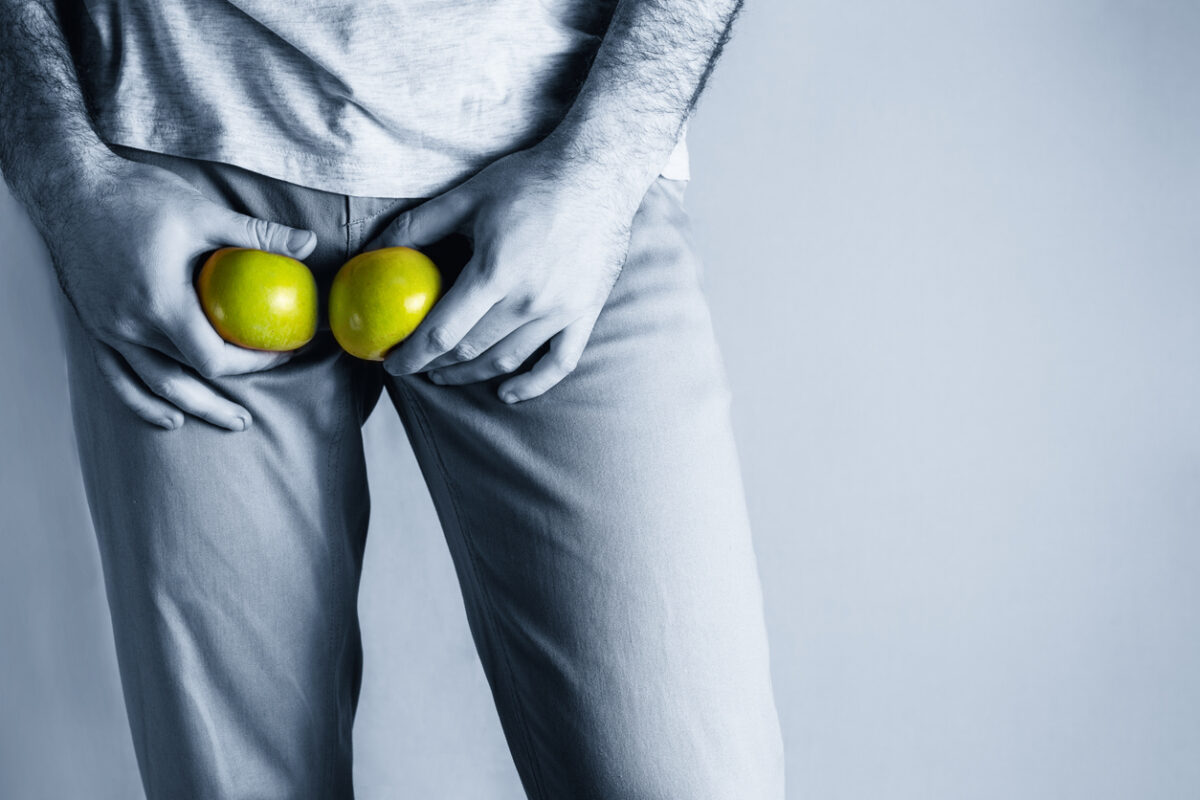 A man in beige jeans at the level of the genitals , holding a ripe and rotten apple. Disease for men. The concept of protection of sexually transmitted infections. Copy space. Blue tint