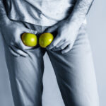 A man in beige jeans at the level of the genitals , holding a ripe and rotten apple. Disease for men. The concept of protection of sexually transmitted infections. Copy space. Blue tint