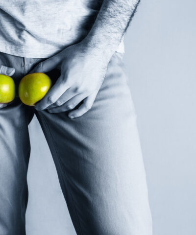 A man in beige jeans at the level of the genitals , holding a ripe and rotten apple. Disease for men. The concept of protection of sexually transmitted infections. Copy space. Blue tint