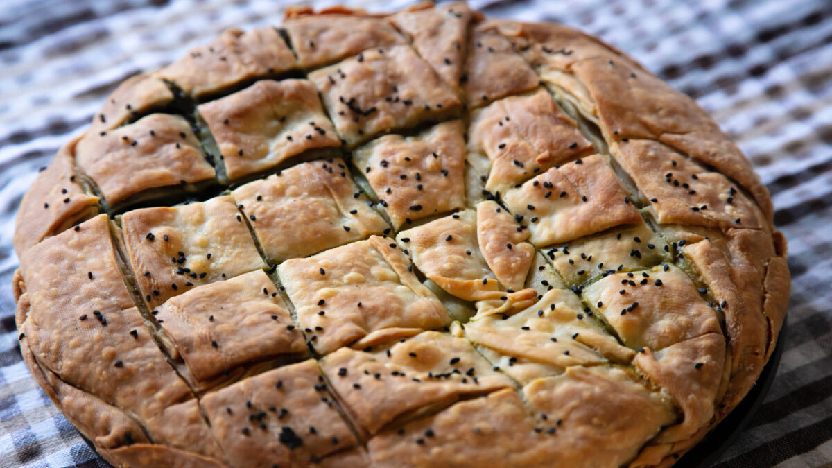 Healthy greek food concept. Whole spinach pie with sesame seeds or greek spanakopita with phyllo on kitchen table background