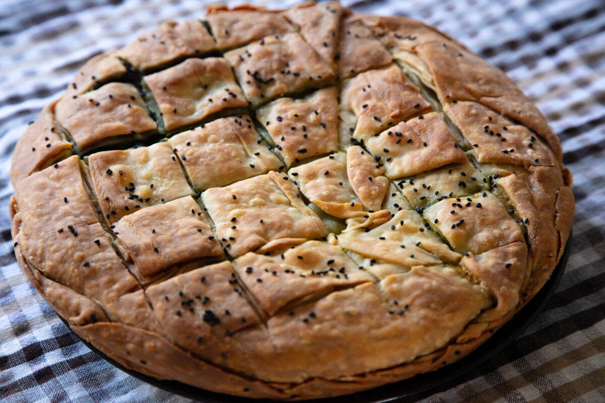 Healthy greek food concept. Whole spinach pie with sesame seeds or greek spanakopita with phyllo on kitchen table background