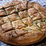 Healthy greek food concept. Whole spinach pie with sesame seeds or greek spanakopita with phyllo on kitchen table background