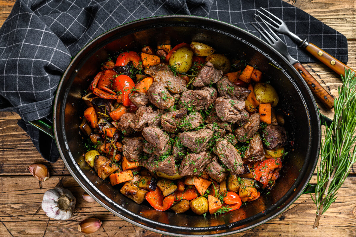 Beef meat stew with potatoes, carrots and herbs. Wooden background