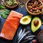Healthy eating: high angle view of a group of food with high levels of Omega-3 fat. The composition includes salmon, sardines, avocado, extra virgin olive oil, and various nuts and seeds like pumpkin seeds, chis seeds, pecan, almonds, pistachio, walnuts and hazelnuts. High resolution 42Mp studio digital capture taken with Sony A7rII and Sony FE 90mm f2.8 macro G OSS lens