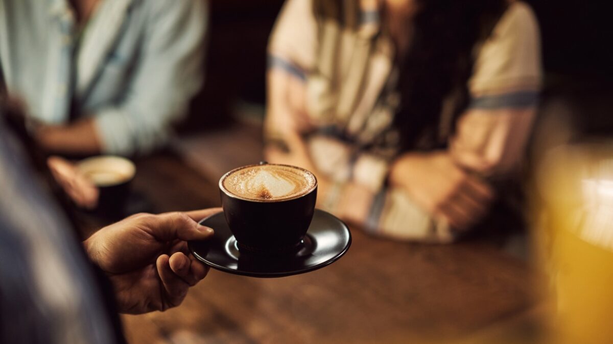 Close-up of waiter serving coffee to customers while working in a cafe.