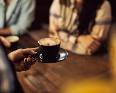 Close-up of waiter serving coffee to customers while working in a cafe.