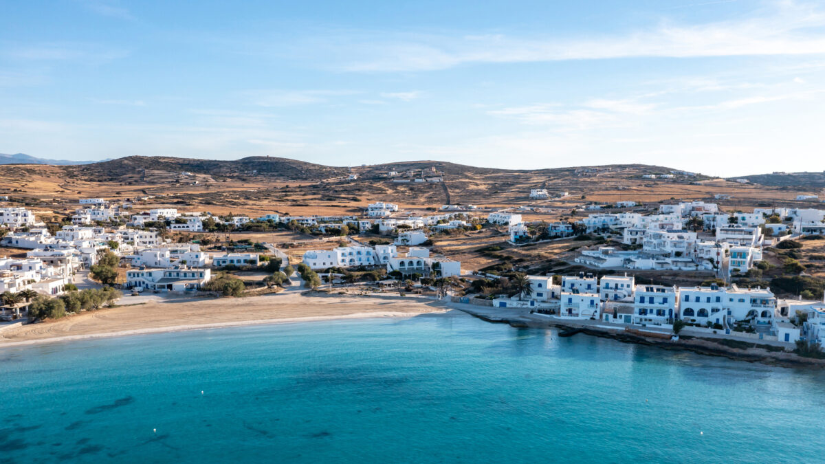 Greece, Koufonisi island, small Cyclades. Aerial drone view. Pano Koufonisi white traditional village buildings, Megali Ammos sandy beach. Calm turquise sea water, clear blue sky background.