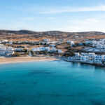 Greece, Koufonisi island, small Cyclades. Aerial drone view. Pano Koufonisi white traditional village buildings, Megali Ammos sandy beach. Calm turquise sea water, clear blue sky background.