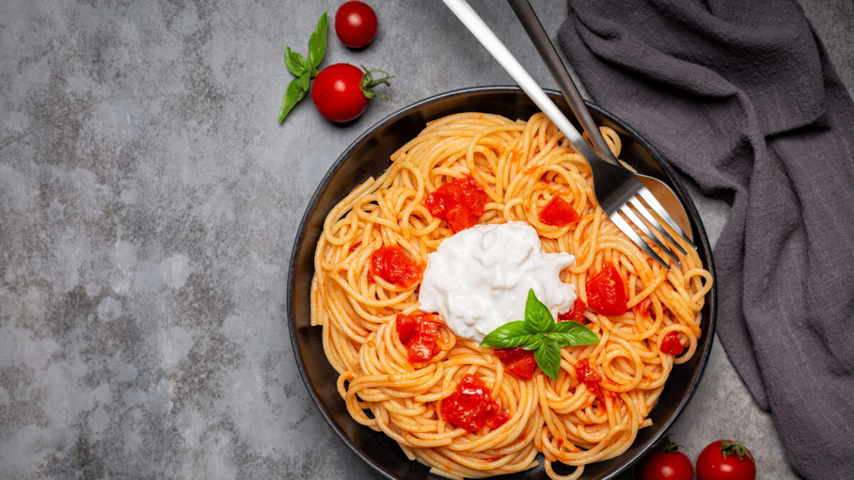 Stracciatella with spaghetti and tomatoes in black dish on dark grey background