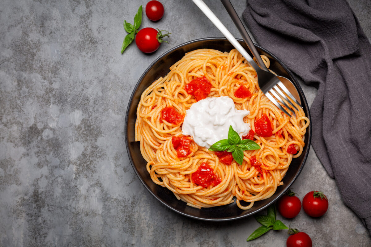 Stracciatella with spaghetti and tomatoes in black dish on dark grey background