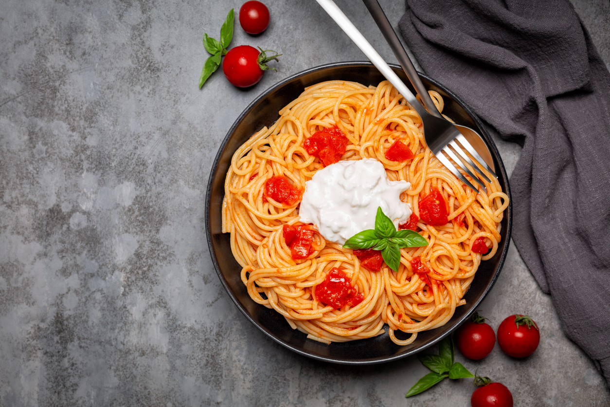 Stracciatella with spaghetti and tomatoes in black dish on dark grey background