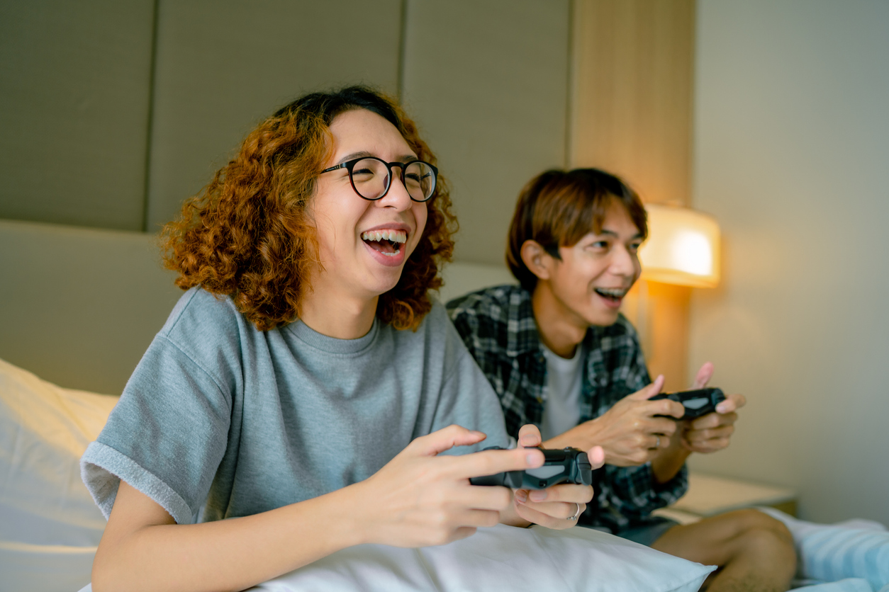 Competitive Asian gay couple laughing and playing games with joysticks on leisure time
