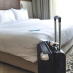 Close up of black luggage and surgical mask. Hotel room bed background, copy space for text, Traveling in new normal lifestyle concept. Stay safe while travel during Covid 19 pandemic concept.