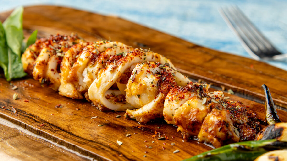 Spicy sliced grilled squid with green pepper and garlic on a wooden serving board