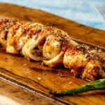 Spicy sliced grilled squid with green pepper and garlic on a wooden serving board