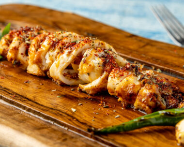 Spicy sliced grilled squid with green pepper and garlic on a wooden serving board