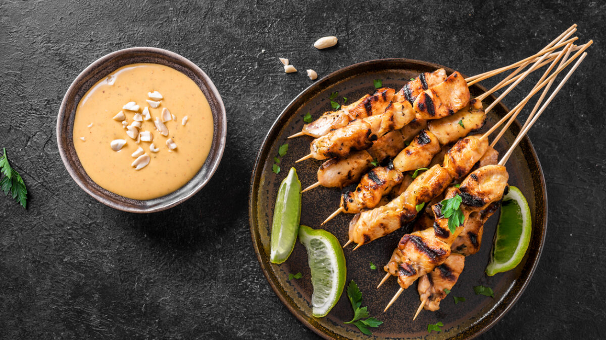 Chicken grilled satay skewers served with lime and peanut sauce on black, top view. Asian thai style food