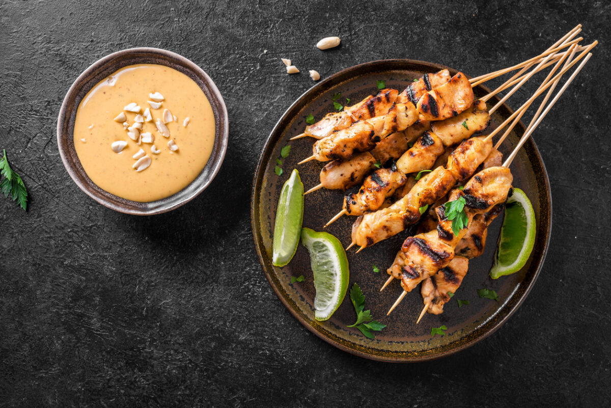 Chicken grilled satay skewers served with lime and peanut sauce on black, top view. Asian thai style food