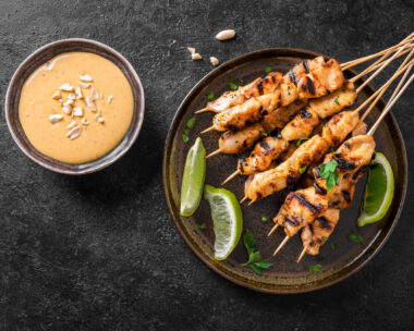Chicken grilled satay skewers served with lime and peanut sauce on black, top view. Asian thai style food