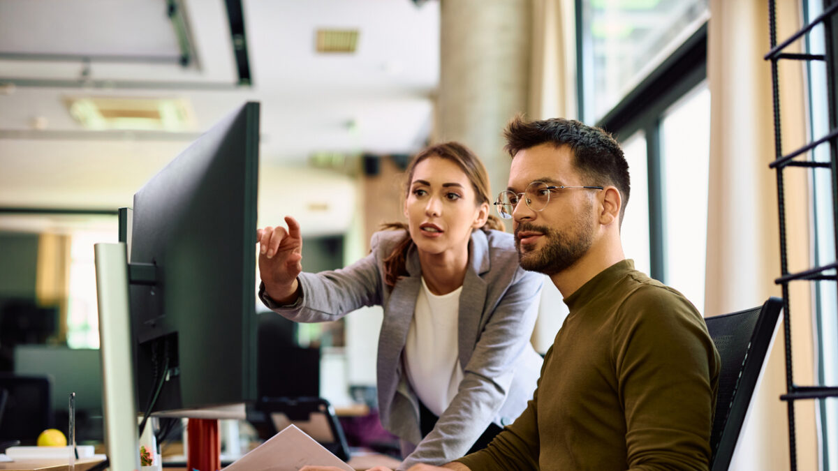 Young entrepreneur and his female coworker using desktop PC while working in the office.