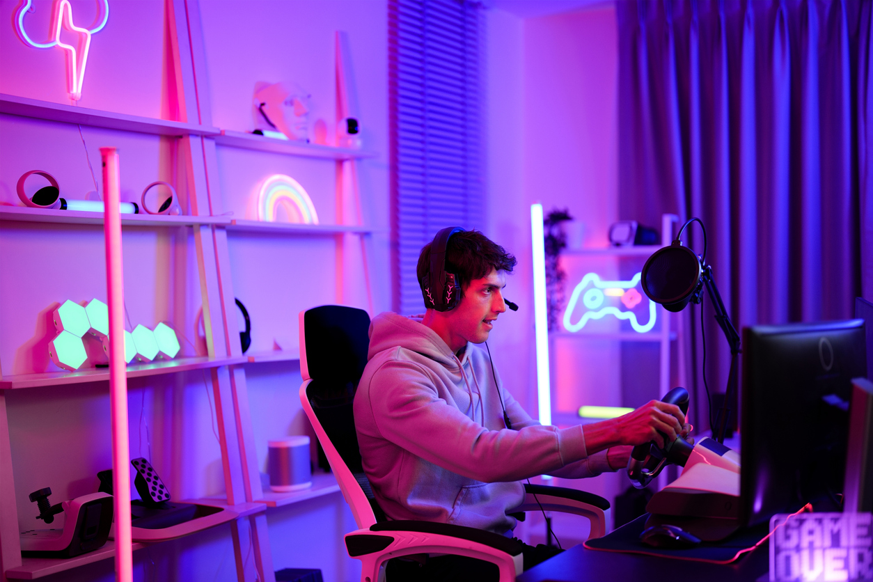 Caucasian handsome teen boy focus to use steering wheel for playing cyber sport racing car game competition online in computer with his close friend at entertainment neon room