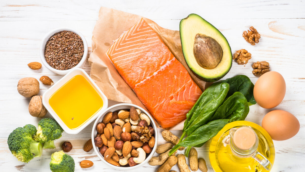 Keto diet product at white wooden table. Salmon, olive oil, avocado, eggs, nuts and vegetables. Healthy food.