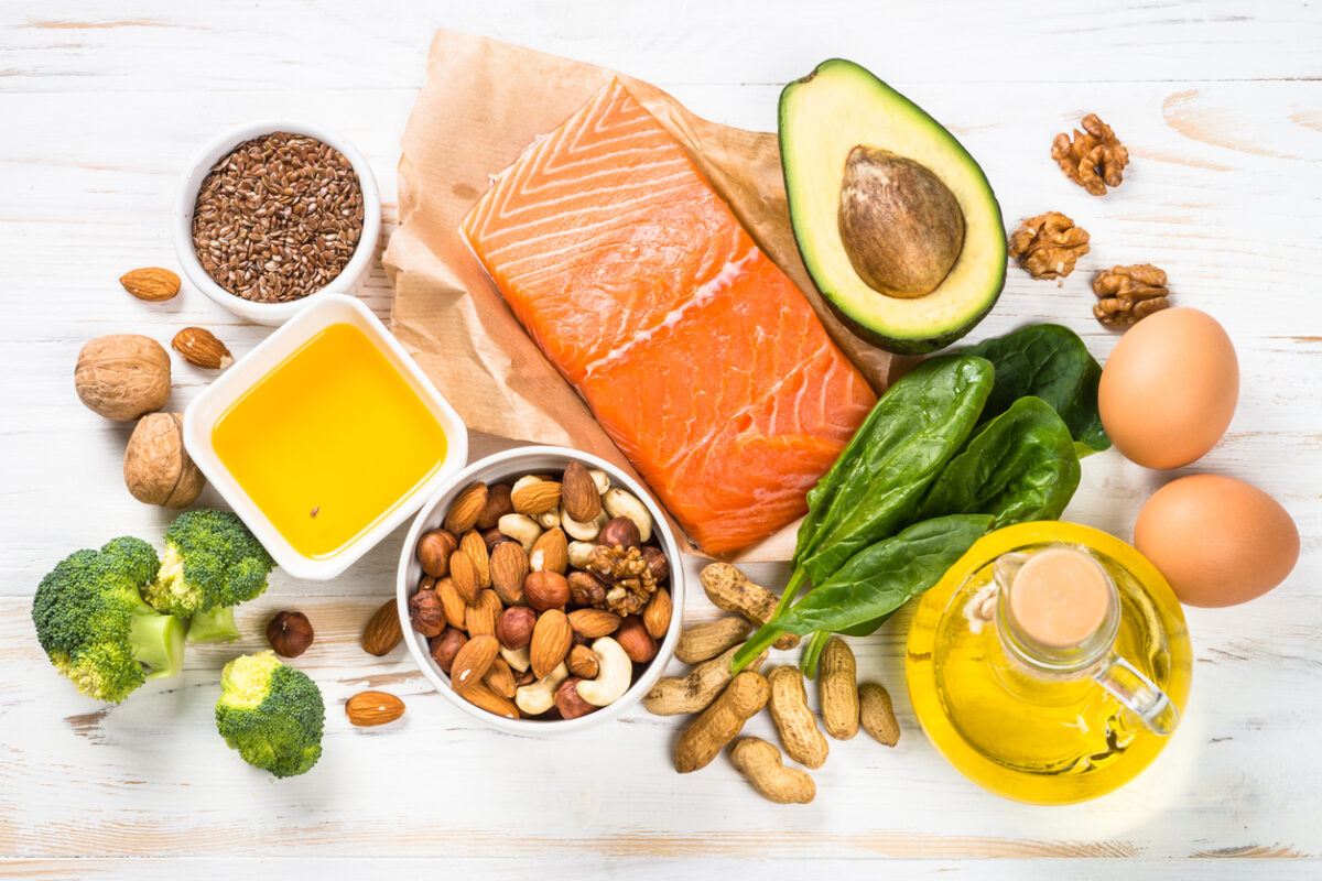 Keto diet product at white wooden table. Salmon, olive oil, avocado, eggs, nuts and vegetables. Healthy food.