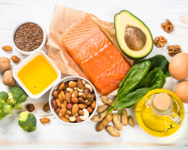 Keto diet product at white wooden table. Salmon, olive oil, avocado, eggs, nuts and vegetables. Healthy food.