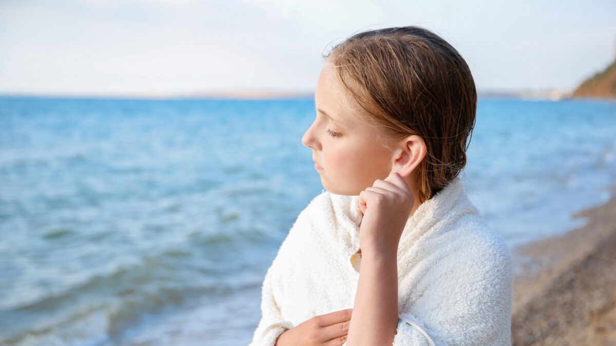 The child got water in his ear while swimming in the sea. The girl cleans her ear from water.