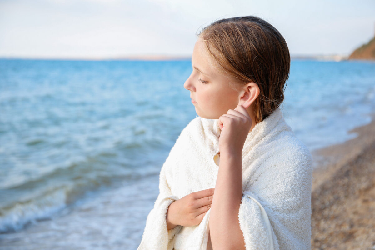 The child got water in his ear while swimming in the sea. The girl cleans her ear from water.