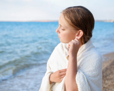 The child got water in his ear while swimming in the sea. The girl cleans her ear from water.