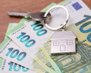 House key symbol pendant on one hundred euro banknotes, fanned out on a wooden desk