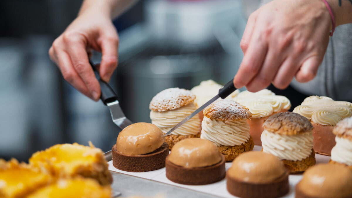 Close-up of a pastry chef's hands meticulously arranging delicious cream puffs and tarts on a tray, showcasing the artistry and precision of dessert making