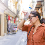 Mature woman suffering from heat stroke in the city, drinking water and touching her forehead. Heat wave in summer sunny days, Eyes closed and hydrating