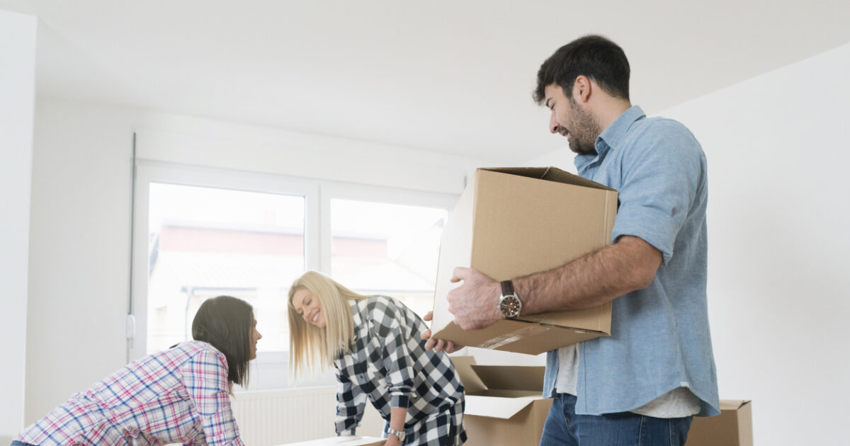Young man carrying a heavy cardboard box while his female friends carrying one box together.