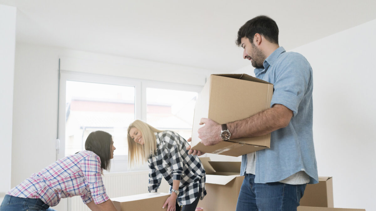 Young man carrying a heavy cardboard box while his female friends carrying one box together.