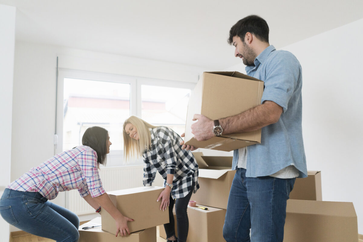 Young man carrying a heavy cardboard box while his female friends carrying one box together.
