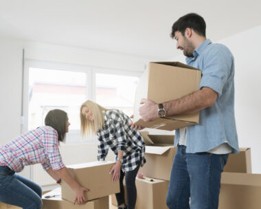 Young man carrying a heavy cardboard box while his female friends carrying one box together.