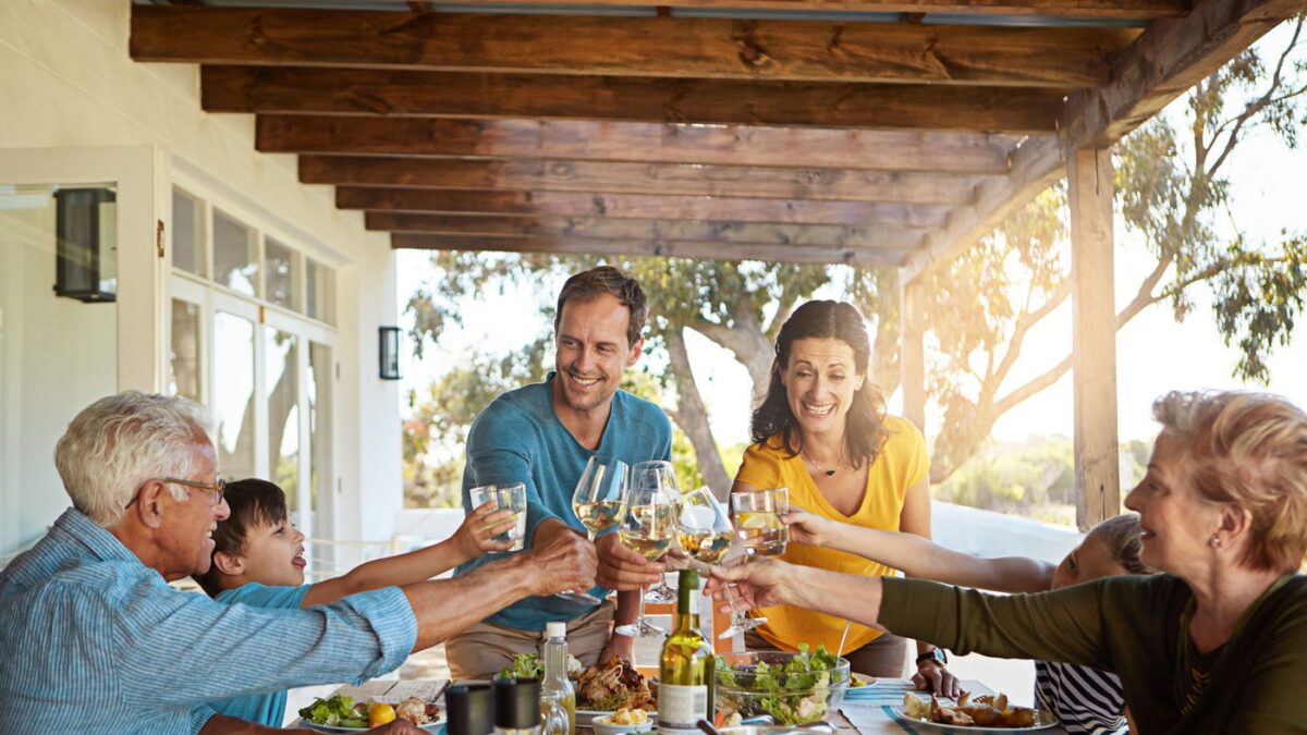 Cheers, wine and family in backyard for food, celebration and eating in happy bonding together at table