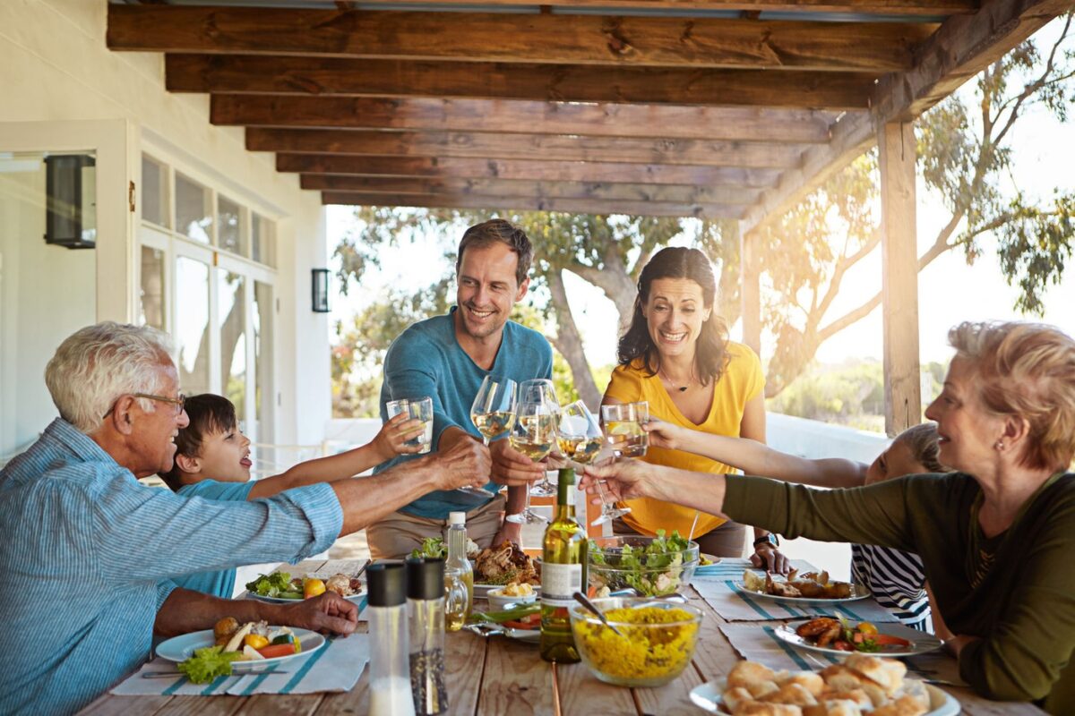 Cheers, wine and family in backyard for food, celebration and eating in happy bonding together at table