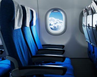 Empty air plane seats. Blue sky and clouds in the window. Airplane interior