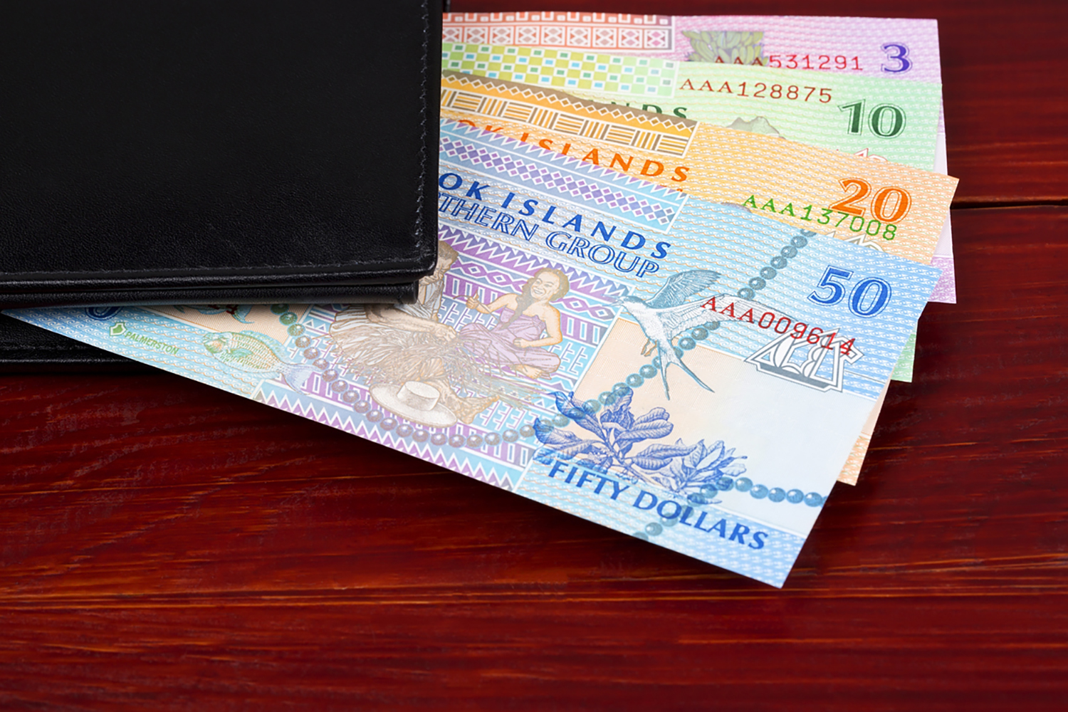 Money from Cook Islands in the black wallet on a wooden background