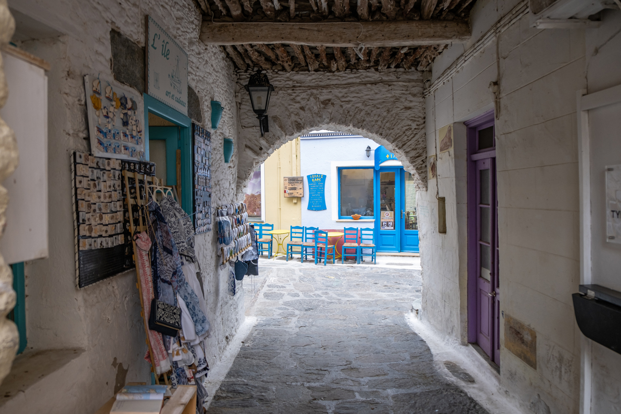 Tzia, Kea island, Cyclades, Greece. January 26, 2020. Traditional coffee shop for relaxing with blue chairs at Ioulis khora town. View from arch stone wall.