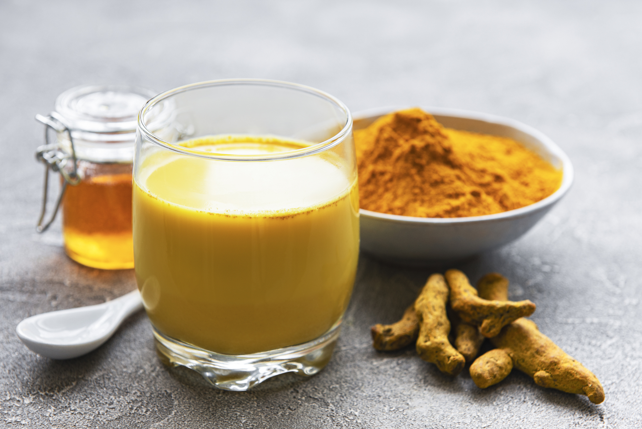 Yellow turmeric latte drink. Golden milk with cinnamon, turmeric, ginger and honey over grey concrete background.