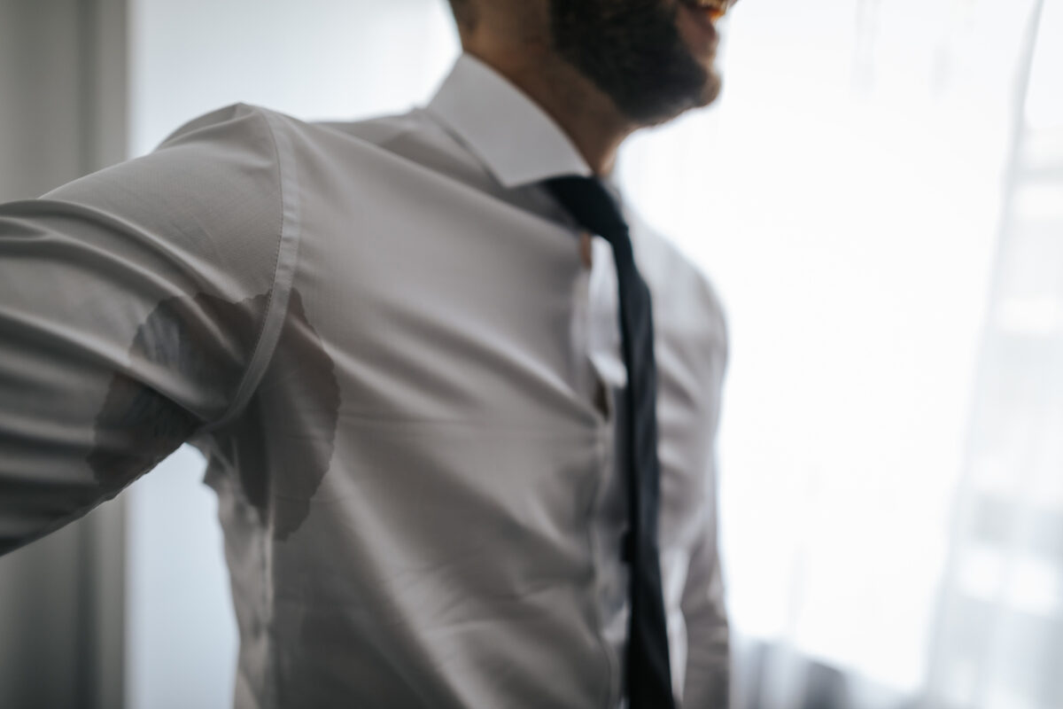 Man with hyperhidrosis sweating under armpit in shirt