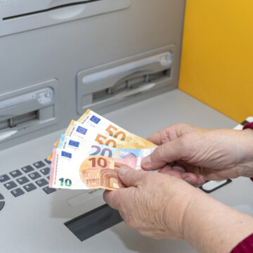 RETIRED SENIOR WOMAN WITHDRAWING MONEY FROM AN ATM. DIGITAL DIVIDE AMONG THE ELDERLY