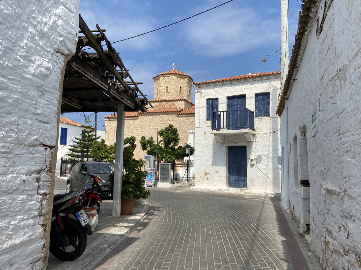 Agistri, Greece - September 13, 2021 : View while driving down a paved road curving past traditional whitewashed buildings and a church in the village of Megalochori on the island of Agistri, Greece