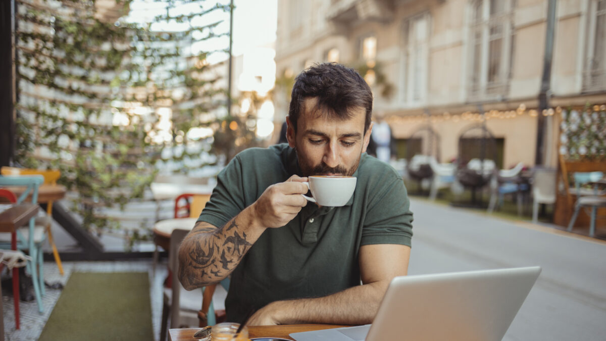 Handsome man enjoying his coffee while working on laptop computer in outside cafeteria