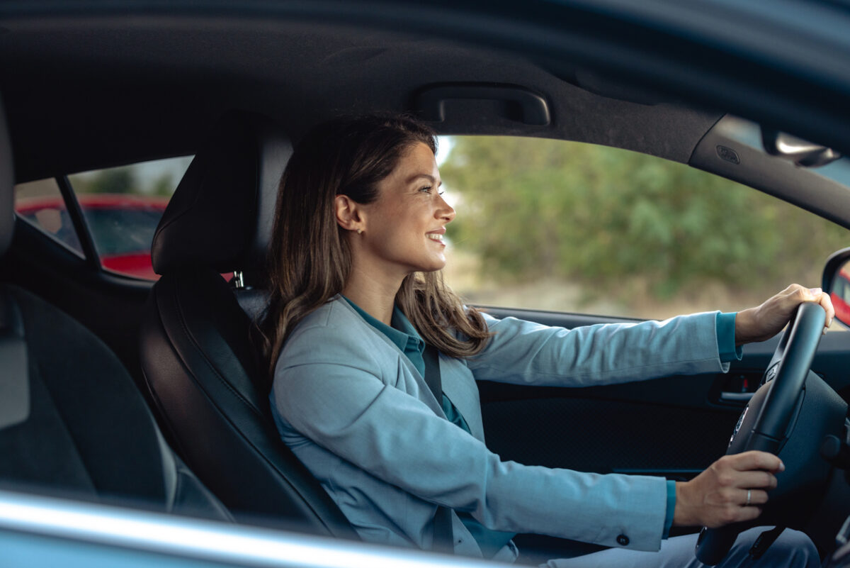 A professional mid-adult woman confidently driving a modern car in an urban setting, showcasing independence and a modern lifestyle.